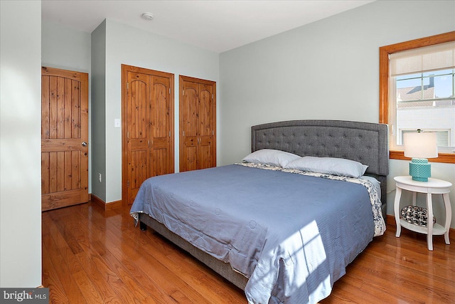 bedroom with multiple closets, baseboards, and wood finished floors