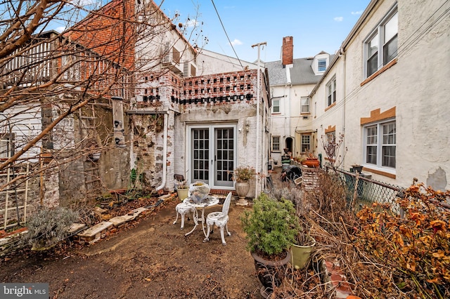 rear view of house with stucco siding, a chimney, fence, and french doors