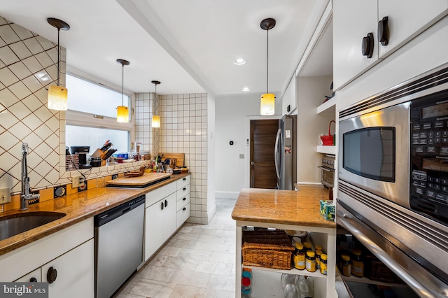 kitchen with tasteful backsplash, white cabinets, appliances with stainless steel finishes, hanging light fixtures, and a sink