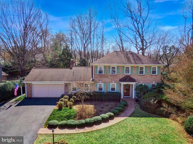 view of front of house with a garage, brick siding, driveway, a front lawn, and a chimney