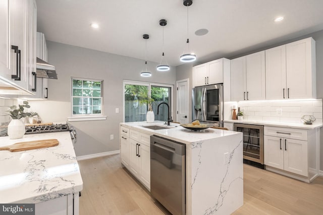 kitchen featuring beverage cooler, decorative backsplash, light wood-style flooring, stainless steel appliances, and a sink