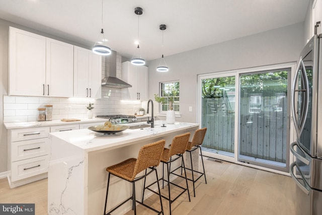 kitchen featuring freestanding refrigerator, white cabinets, a sink, wall chimney range hood, and light wood-type flooring