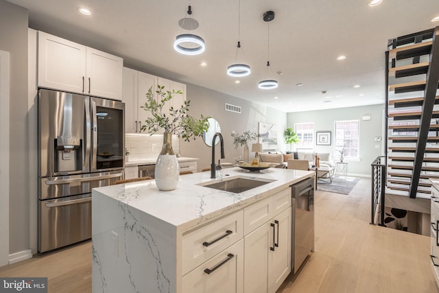 kitchen featuring stainless steel appliances, hanging light fixtures, a kitchen island with sink, a sink, and light wood-type flooring