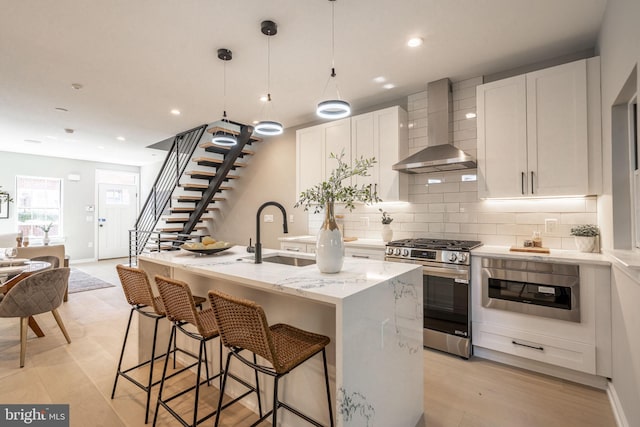 kitchen with gas stove, white cabinetry, a sink, and wall chimney exhaust hood