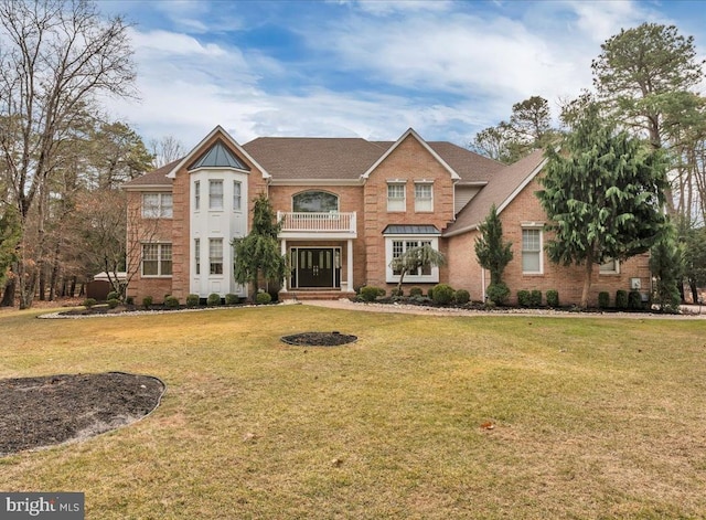 colonial house featuring a front yard, brick siding, and a balcony