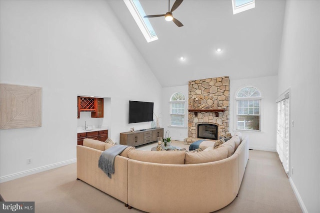 carpeted living room featuring a ceiling fan, a sink, a stone fireplace, high vaulted ceiling, and wet bar