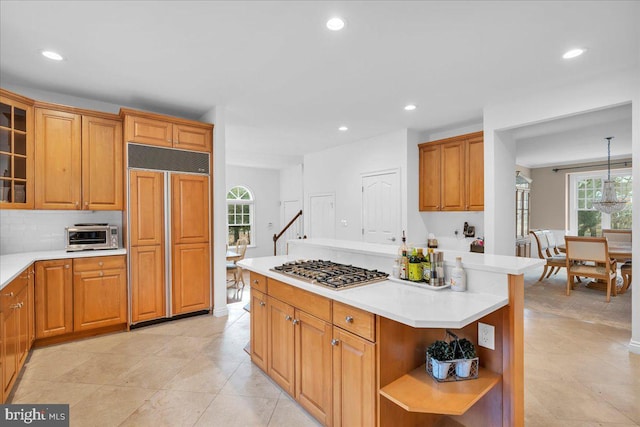 kitchen with paneled built in fridge, stainless steel gas stovetop, open shelves, and light countertops