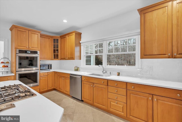 kitchen featuring tasteful backsplash, light countertops, appliances with stainless steel finishes, glass insert cabinets, and a sink