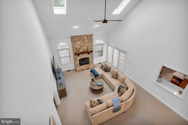 carpeted living room featuring ceiling fan, high vaulted ceiling, a stone fireplace, a skylight, and baseboards