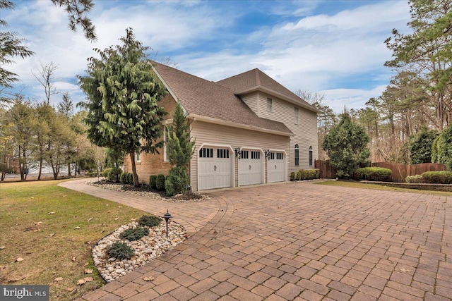 view of property exterior featuring decorative driveway, fence, an attached garage, and a lawn