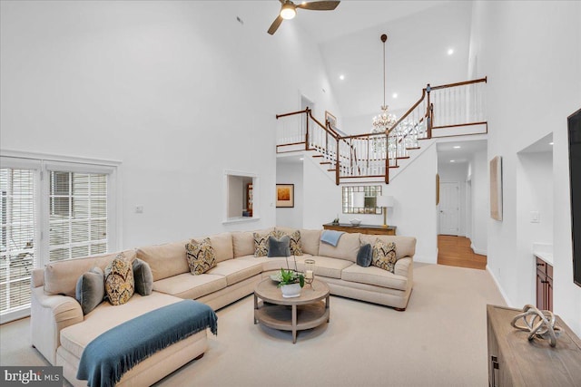 living area featuring stairs, ceiling fan with notable chandelier, a towering ceiling, and baseboards