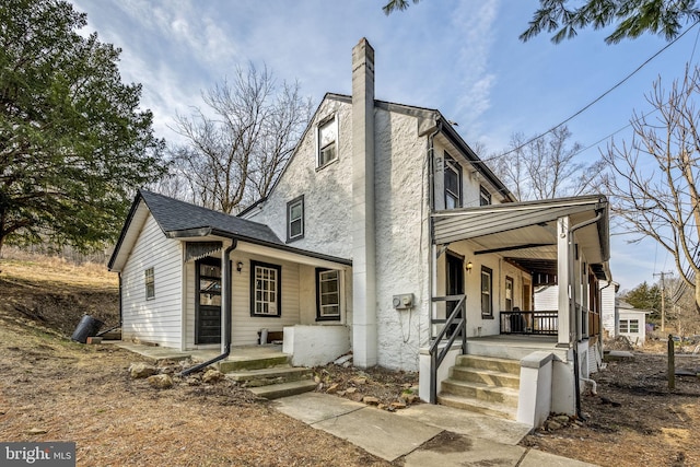 view of front of property with stucco siding, a porch, a chimney, and a shingled roof