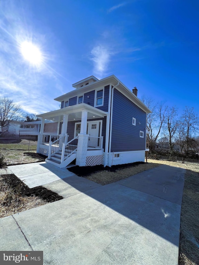 traditional style home featuring a porch, a chimney, and driveway