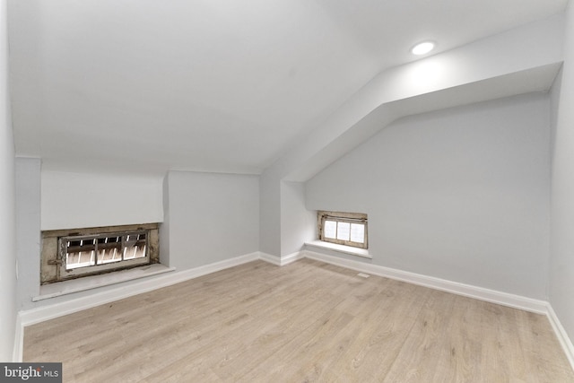 additional living space with a fireplace, baseboards, vaulted ceiling, and wood finished floors