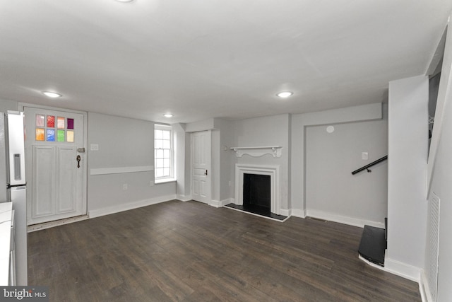 unfurnished living room with a fireplace with raised hearth, dark wood finished floors, visible vents, and baseboards