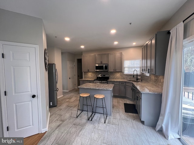 kitchen with tasteful backsplash, appliances with stainless steel finishes, a center island, gray cabinetry, and a sink