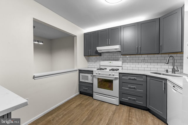 kitchen with white appliances, under cabinet range hood, a sink, and gray cabinetry