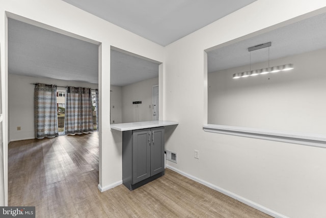 kitchen featuring decorative light fixtures, light countertops, gray cabinetry, wood finished floors, and baseboards