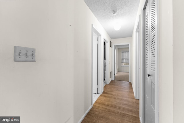 corridor featuring a textured ceiling, wood finished floors, and baseboards