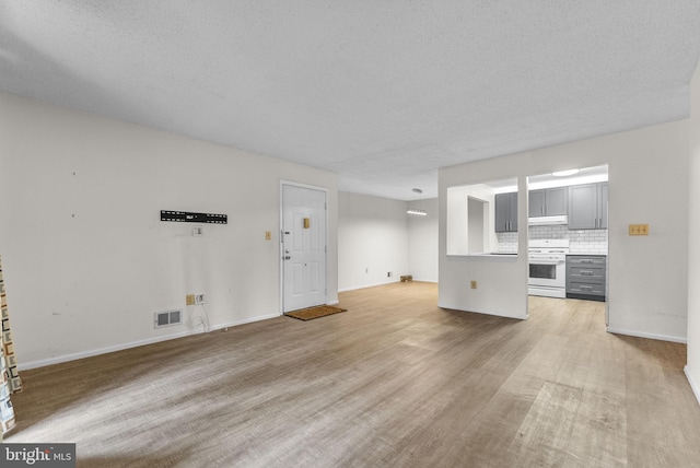 unfurnished living room featuring a textured ceiling, light wood-style flooring, visible vents, and baseboards