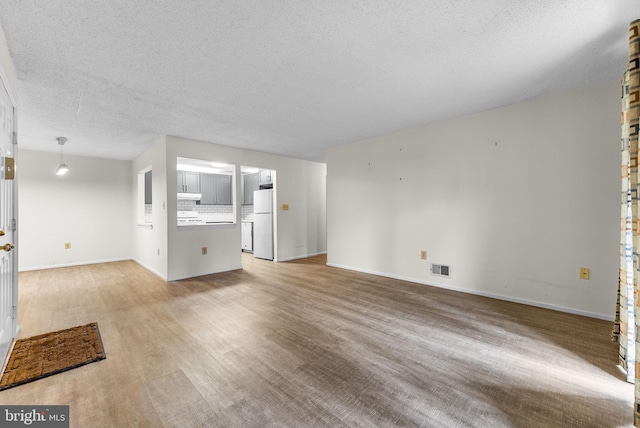 unfurnished living room with light wood-type flooring, visible vents, a textured ceiling, and baseboards