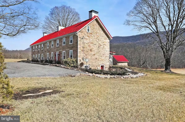 view of side of home featuring stone siding, a lawn, a chimney, and metal roof