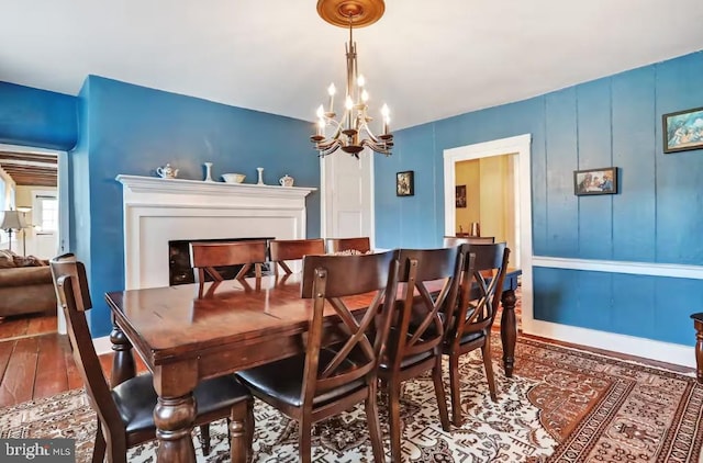 dining area featuring a chandelier, a fireplace, baseboards, and wood finished floors