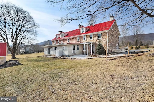 back of house with central AC, a lawn, a chimney, a patio area, and stone siding