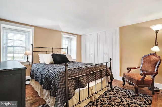 bedroom with multiple windows, baseboard heating, and wood finished floors