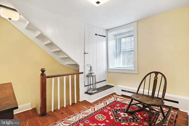 sitting room featuring a baseboard heating unit, stairway, wood finished floors, and baseboards