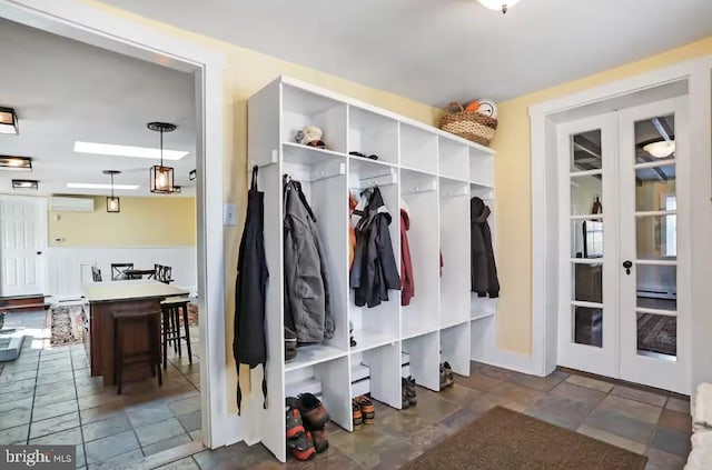 mudroom featuring stone finish flooring, french doors, and a wall unit AC