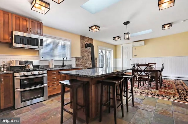 kitchen featuring a wall unit AC, a wainscoted wall, stainless steel appliances, stone finish floor, and a kitchen breakfast bar