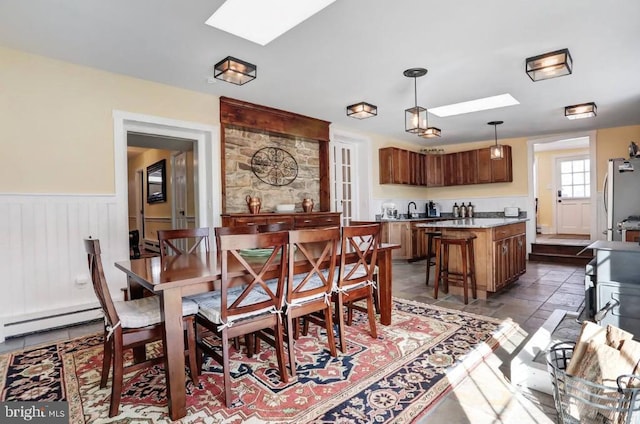 dining area featuring baseboard heating, a skylight, and a wainscoted wall