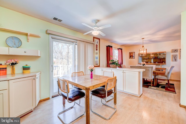 dining room with light wood-type flooring, baseboards, visible vents, and ceiling fan with notable chandelier