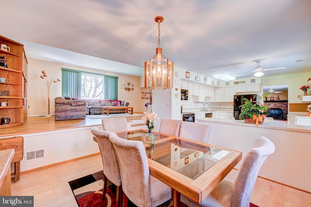 dining space featuring light wood-style floors, ceiling fan, visible vents, and baseboards