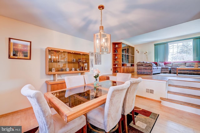 dining space with baseboards, wood finished floors, visible vents, and an inviting chandelier