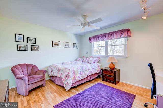 bedroom featuring rail lighting, wood finished floors, a ceiling fan, and baseboards