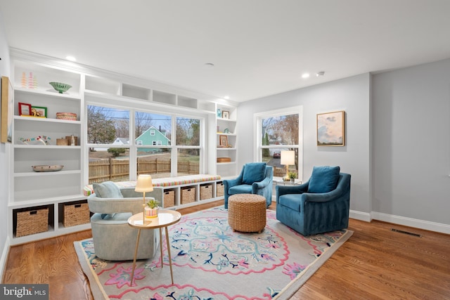 sitting room with built in shelves, recessed lighting, wood finished floors, visible vents, and baseboards