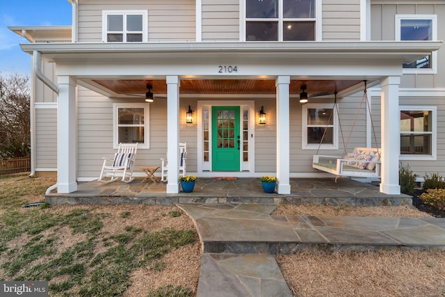 doorway to property featuring board and batten siding, covered porch, and a ceiling fan