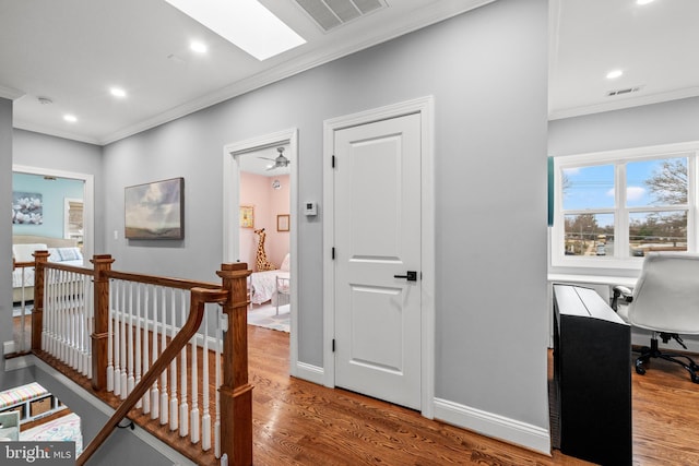 corridor featuring visible vents, ornamental molding, wood finished floors, and an upstairs landing