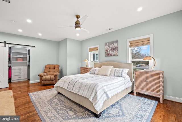 bedroom with baseboards, a barn door, visible vents, and wood finished floors