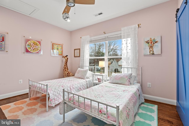 bedroom with a barn door, wood finished floors, visible vents, and baseboards