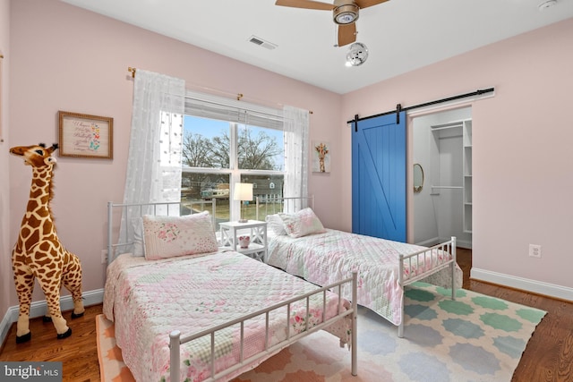 bedroom with a barn door, baseboards, visible vents, a ceiling fan, and wood finished floors