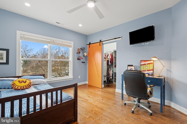 bedroom with visible vents, a spacious closet, a barn door, light wood-type flooring, and baseboards