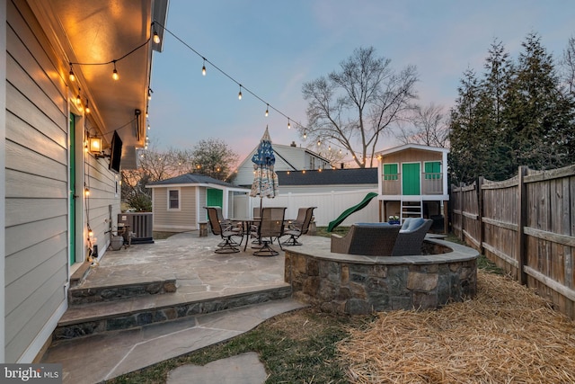 patio terrace at dusk with a fenced backyard, central AC unit, and an outdoor structure