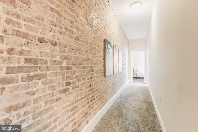 corridor with carpet floors, brick wall, and baseboards