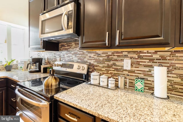 kitchen with stainless steel appliances, light stone countertops, dark brown cabinetry, and decorative backsplash