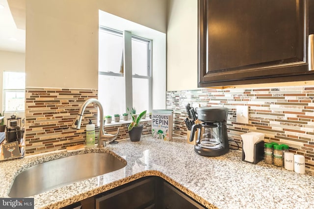 kitchen with tasteful backsplash, a sink, dark brown cabinets, and light stone countertops