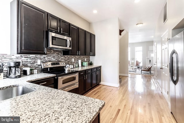 kitchen featuring light stone counters, appliances with stainless steel finishes, light wood-style flooring, and tasteful backsplash