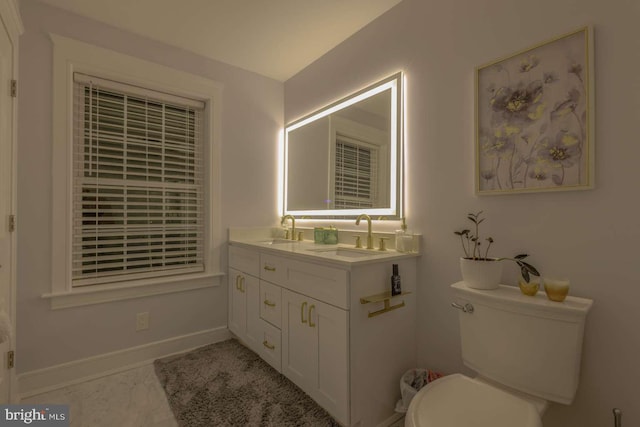 bathroom with toilet, double vanity, baseboards, and a sink